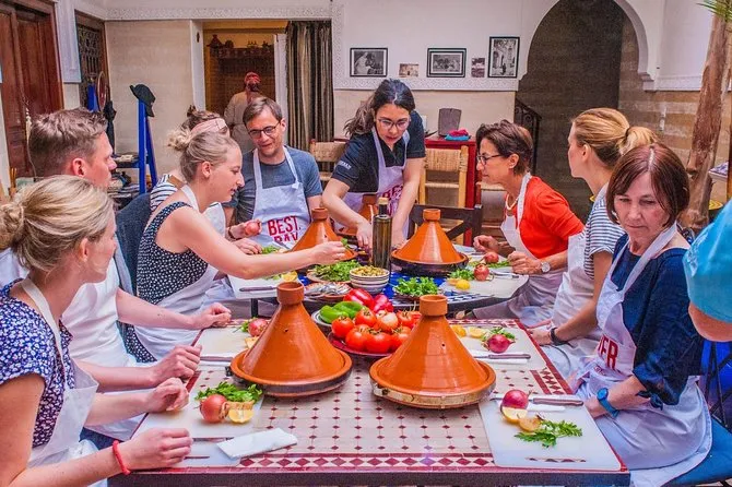 A group in aprons preparing vegetables around a table set with tajines at a Moroccan cooking class