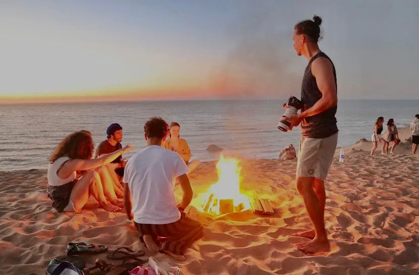 Guests sitting around a bonfire on the beach as the sun sets over the Atlantic