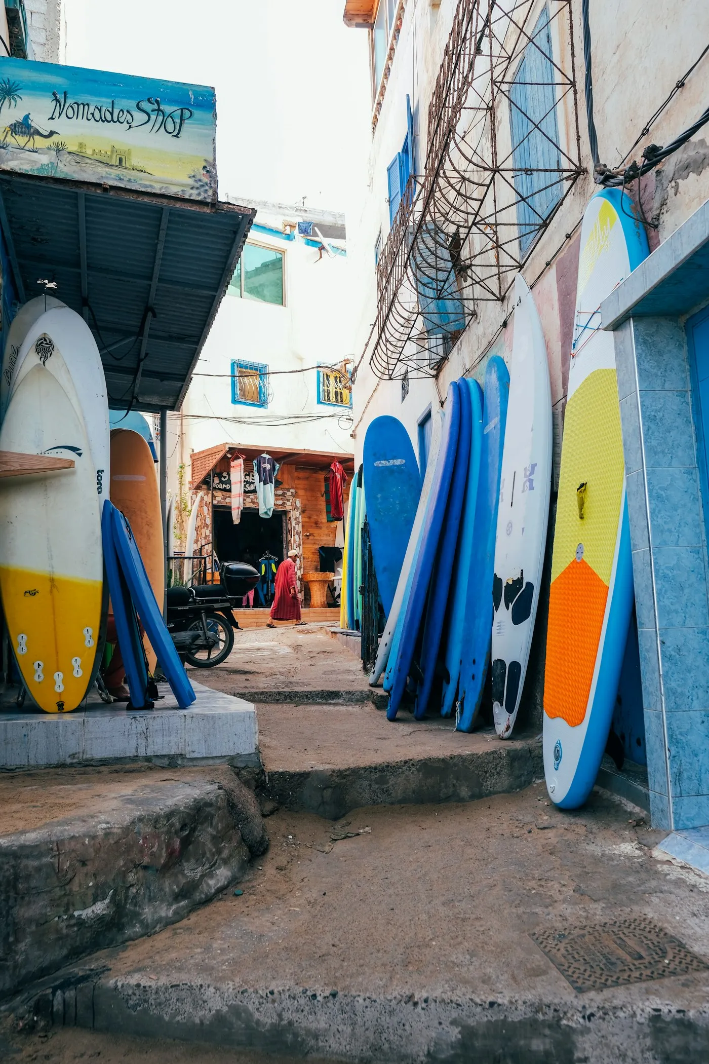Surfboards stacked in a blue-washed alleyway in Taghazout