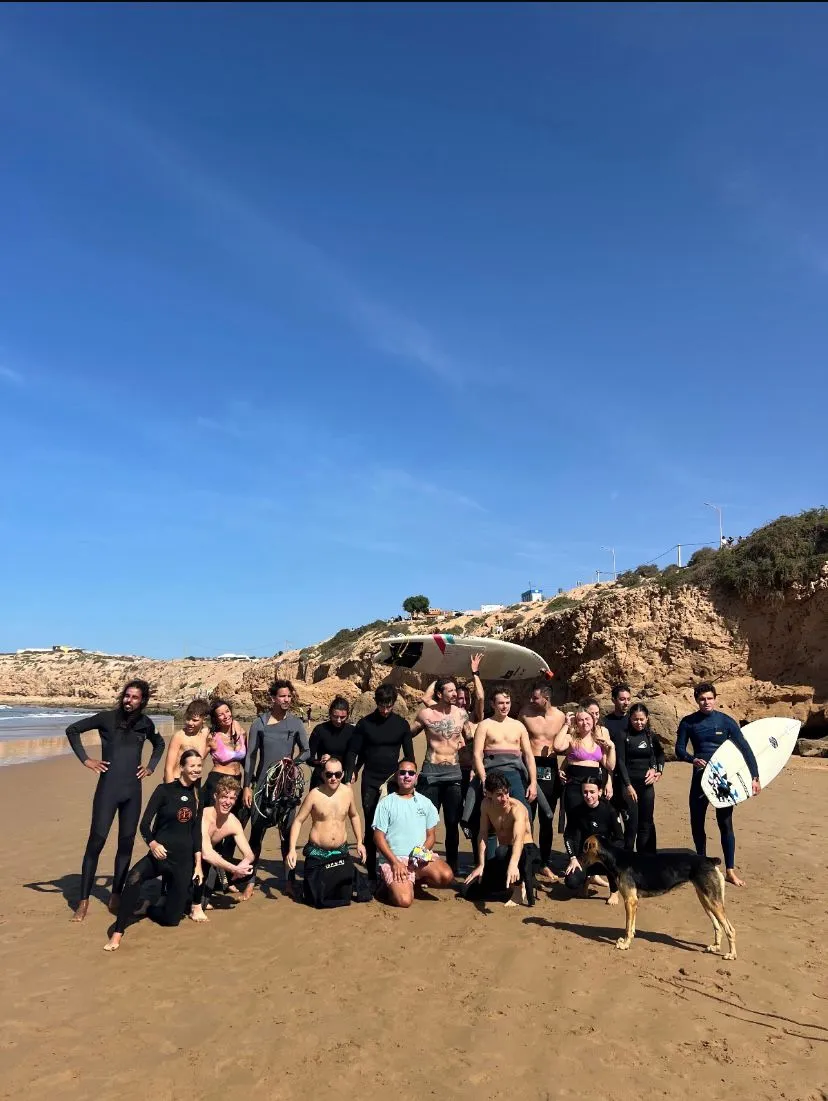 The whole camp gathered on the beach in wetsuits with their boards and a dog, cliffs and blue sky behind