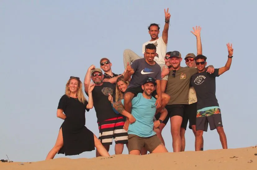 A group of guests standing on top of a sand dune with their arms in the air at golden hour